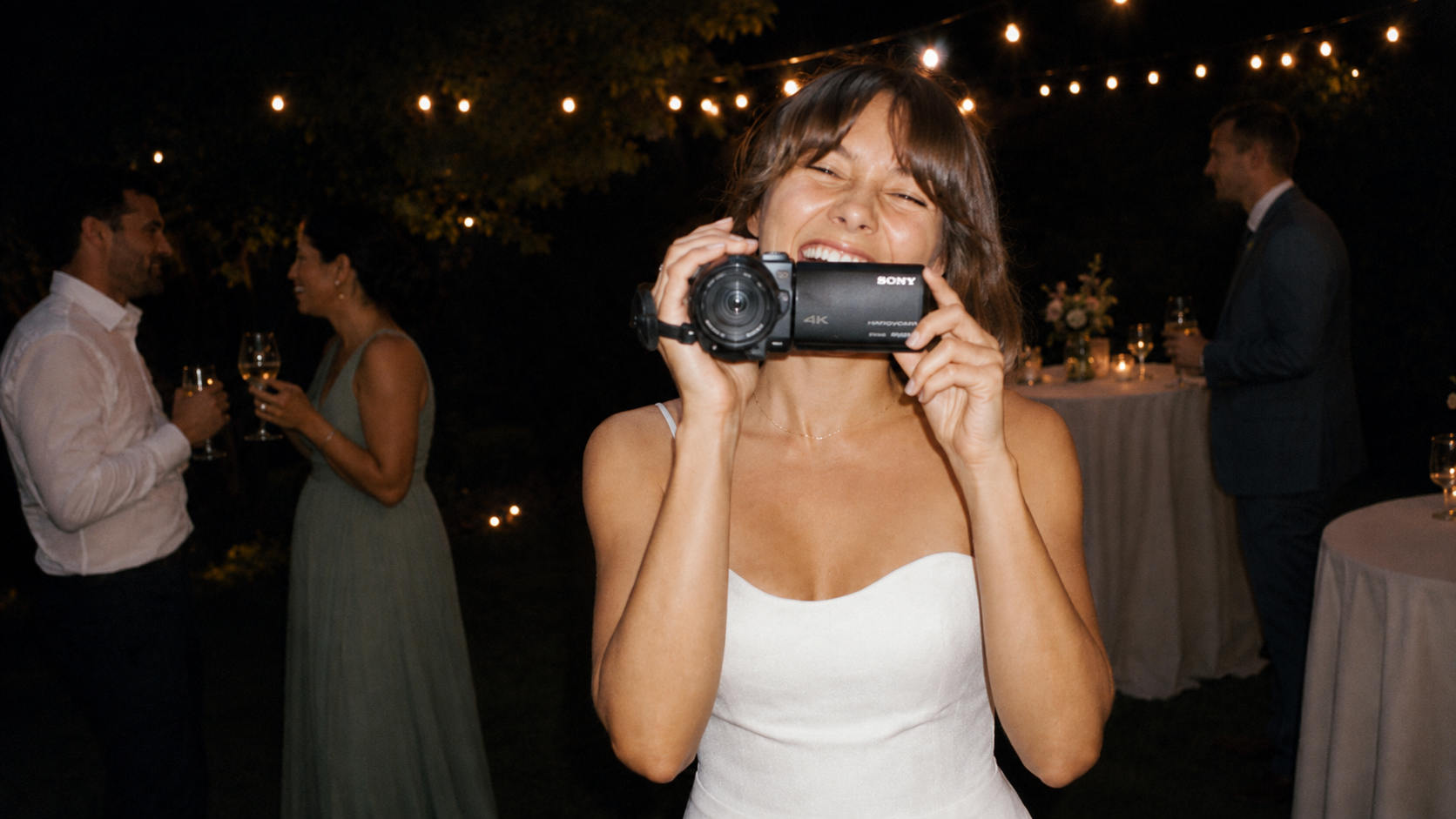 A wedding guest holding a handheld camcorder, filming candid moments from inside the celebration.